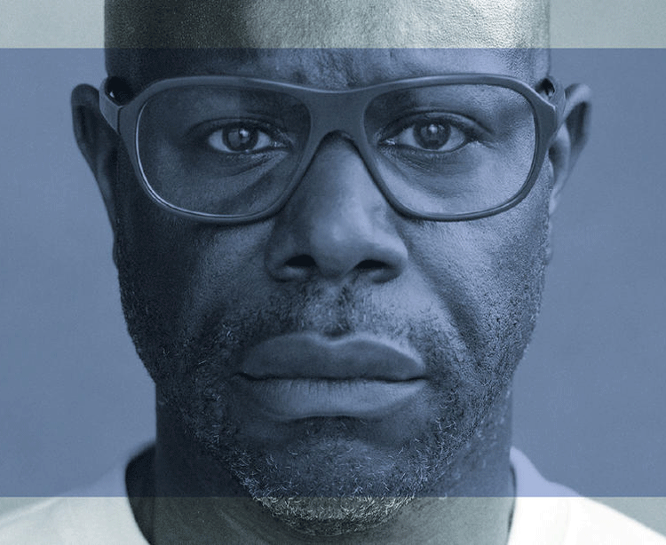 a man wearing a white t-shirt and dark glasses stares into the camera