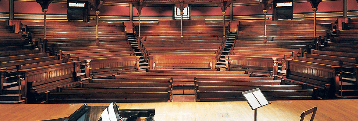 interior view of the semicircular wooden mezzanine and orchestra in Sanders Theatre, with a grand piano and music stand on stage