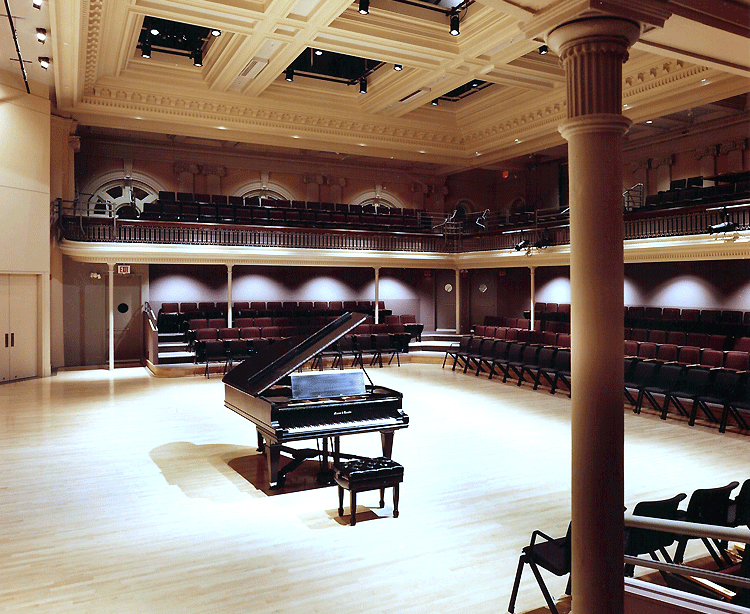 stage right view of the rectangular wooden orchestra and mezzanine in Lowell Hall, with a grand piano center stage